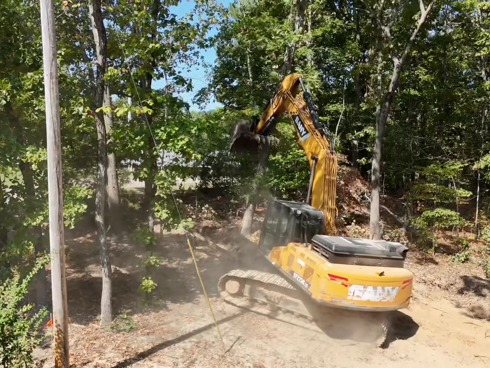 An excavator pushing a tree over in a cloud of dust.